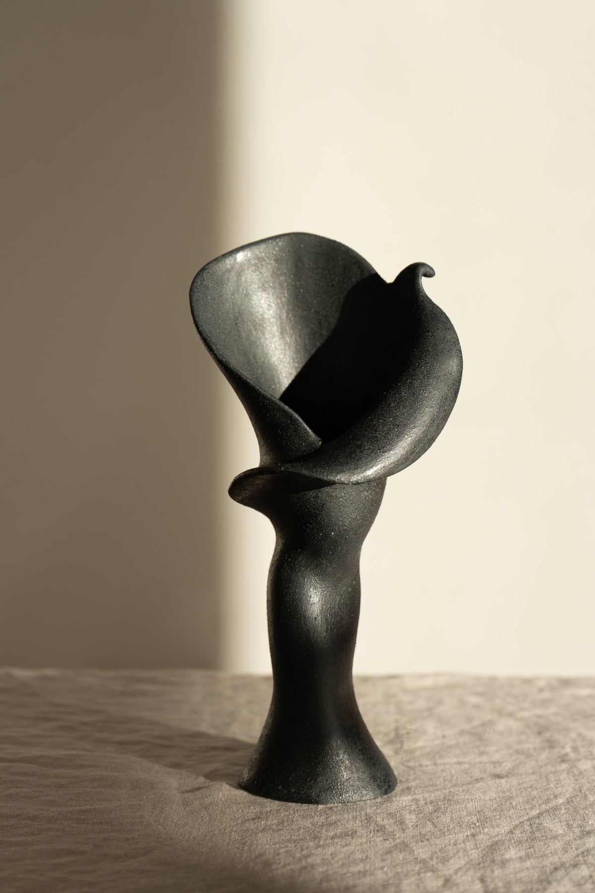  A matte black ceramic vase inspired by the Calla Lily, blending floral curves with bold stoneware. Features a glazed interior, perfect as a striking modern decor piece.