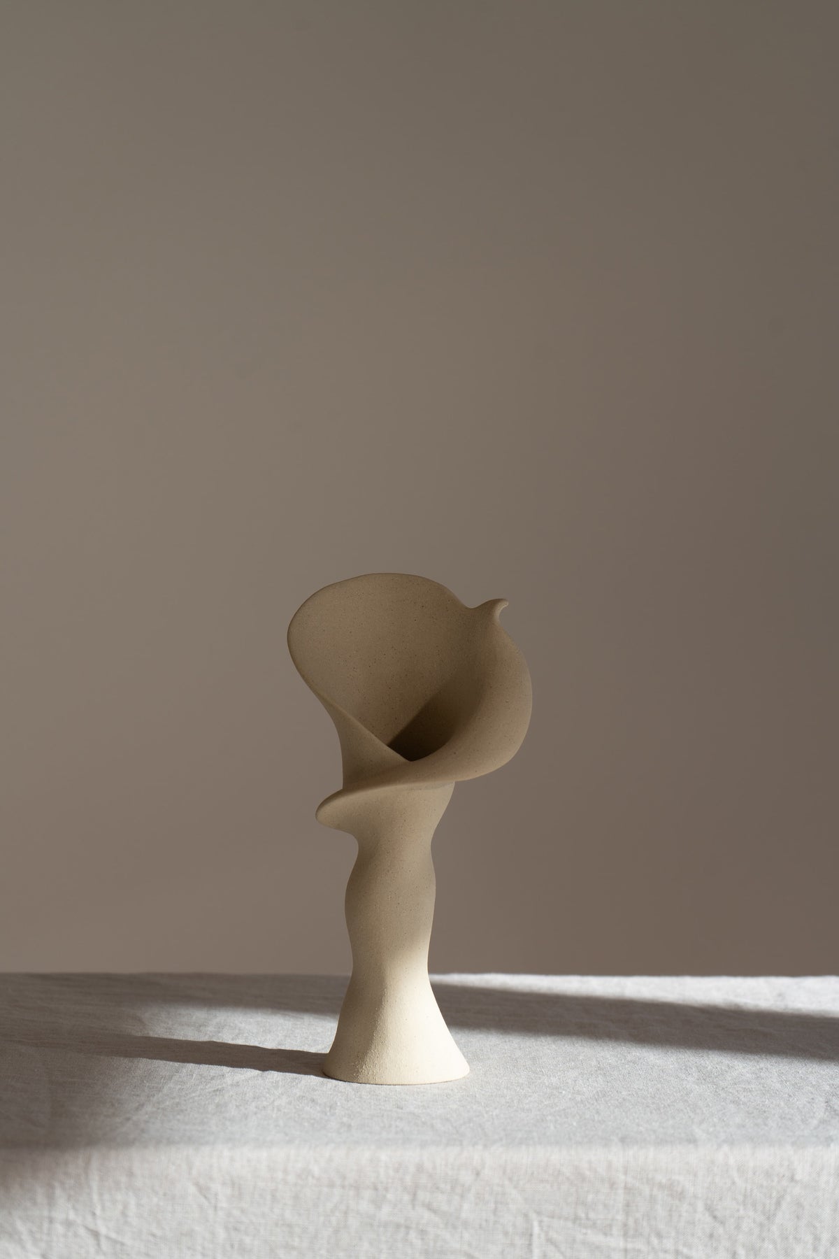A matte taupe ceramic vase inspired by the Calla Lily, combining bold stoneware with soft floral curves. 