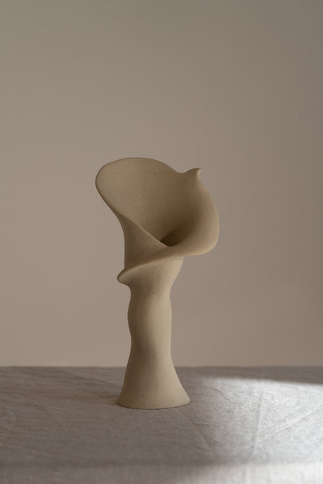 A matte taupe ceramic vase inspired by the Calla Lily, combining bold stoneware with soft floral curves. 